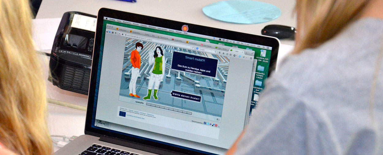 Schülerinnen betrachten auf einem Laptop eine Website zum Thema Digitalisierung.